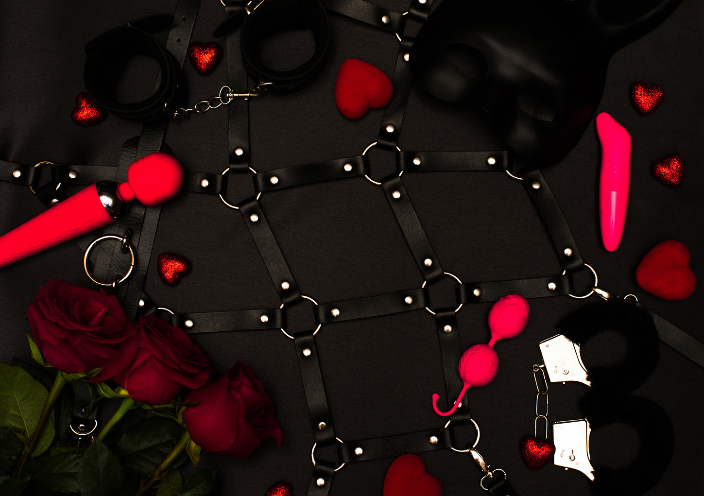 Various sex toys set on a black background. An ad for a sex shop. Top view. Spring. Roses.